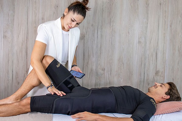 Client receiving EMS therapy while practitioner adjusts thigh electrode